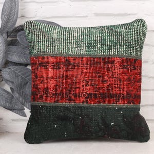 May include: A rectangular cushion with a patchwork design. The top section is green and white striped, the middle is red, and the bottom is dark green. The cushion is made of a textured fabric.