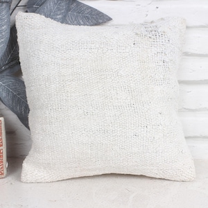 May include: White throw pillow with a textured woven fabric. The pillow is square and has a simple design.