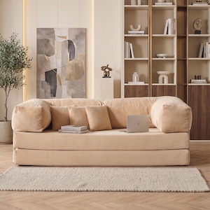May include: A beige corduroy sofa with matching throw pillows and a laptop. The sofa sits on a light beige rug, with a wooden floor in the foreground. A modern living room setting with a neutral color palette.