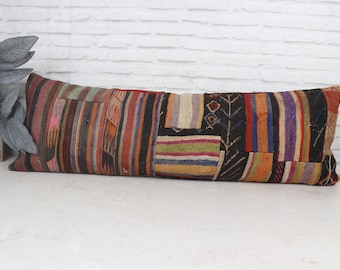 Op de afbeelding: Een lang, rechthoekig patchwork kussen met een verscheidenheid aan kleuren en patronen, waaronder rood, oranje, geel, groen, blauw, paars en zwart. Het kussen is gemaakt van geweven stof en heeft een gefranst randje.