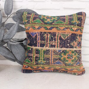 May include: A decorative pillow with a colorful geometric pattern in shades of orange, green, blue, and black. The pillow is made of woven fabric and has a fringed edge.