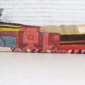 May include: A long, rectangular patchwork pillow with a variety of colors and patterns, including red, brown, yellow, and blue. The pillow is made of woven fabric and has a fringed edge.
