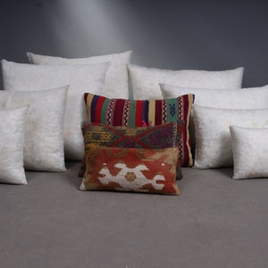 May include: A collection of decorative pillows and pillow inserts. The pillows are in various shapes and sizes, with white inserts and patterned covers in red, green, and gold. The pillows are arranged on a gray surface.
