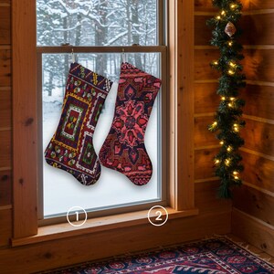 Pu&ograve; includere: Due calze di Natale decorate sono appese davanti a una finestra innevata. Una &egrave; principalmente bordeaux con disegni geometrici verdi, gialli e bianchi. L'altra &egrave; rossa con un motivo floreale. Una ghirlanda con luci decora la parete di legno.