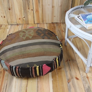 May include: A round, floor cushion with a patchwork design. The cushion features a mix of brown, tan, and green stripes and patterns. The edges are trimmed with colorful fabric. The cushion is approximately 30 inches in diameter.