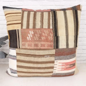 Könnte beinhalten: Ein quadratisches Patchwork-Kissen in neutralen Farbtönen. Das Design umfasst verschiedene Stoffe mit Streifen und geometrischen Mustern in Beige, Braun und Creme. Ein dekorativer Artikel für ein Bett oder Sofa, ca. 40 cm x 40 cm.