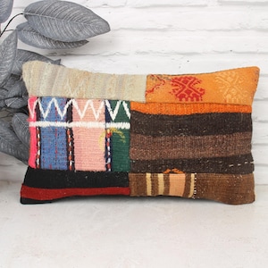 Può includere: Un cuscino rettangolare in patchwork con una varietà di colori e motivi, tra cui arancione, marrone, rosa, blu e bianco. Il cuscino è realizzato in tessuto tessuto e ha un aspetto rustico e fatto a mano.