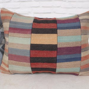May include: A striped throw pillow with a patchwork design in shades of red, blue, beige, and black. The pillow is made of woven fabric and has a rectangular shape.