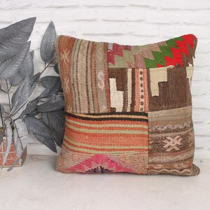 Op de afbeelding: Een patchwork kussenhoes met verschillende kleuren en texturen, waaronder bruin, rood, groen en roze. De kussenhoes is gemaakt van geweven stof en heeft een vierkante vorm.