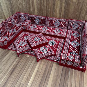 May include: A modular floor seating set featuring a deep red fabric with a repeating white and black geometric pattern. The set includes long rectangular floor cushions, backrest cushions, square floor pillows, and a central square ottoman.
