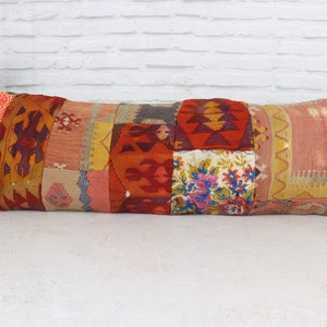 May include: A long, rectangular patchwork pillow with a variety of colors and patterns, including red, orange, yellow, and blue. The pillow is made of woven fabric and has a fringed edge.