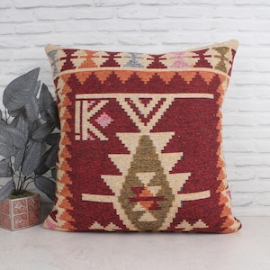 May include: A red, orange, and beige patterned throw pillow with a geometric design. The pillow is made of woven fabric and has a fringe border.