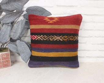 May include: Multicolored striped throw pillow with a geometric pattern. The pillow is made of woven fabric and has a red, black, yellow, and blue color scheme.