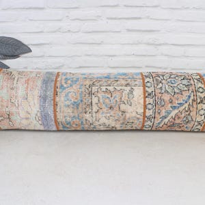 May include: A long, rectangular cushion with a patchwork design. The cushion is made of a beige fabric with a floral pattern and has a brown border. The cushion is ideal for adding a touch of bohemian style to any room.