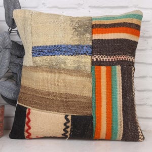 Peut inclure: Coussin carré décoratif avec un design patchwork. Le coussin présente divers tissus texturés en beige, marron, noir, orange et bleu. Le design comprend des rayures et des motifs géométriques, créant une esthétique rustique et chaleureuse.