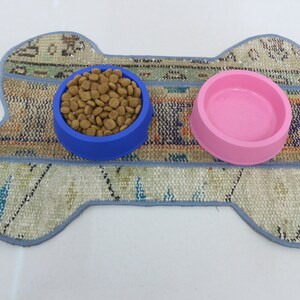 May include: A bone-shaped pet feeding mat with a blue bowl filled with dog food and a pink water bowl.