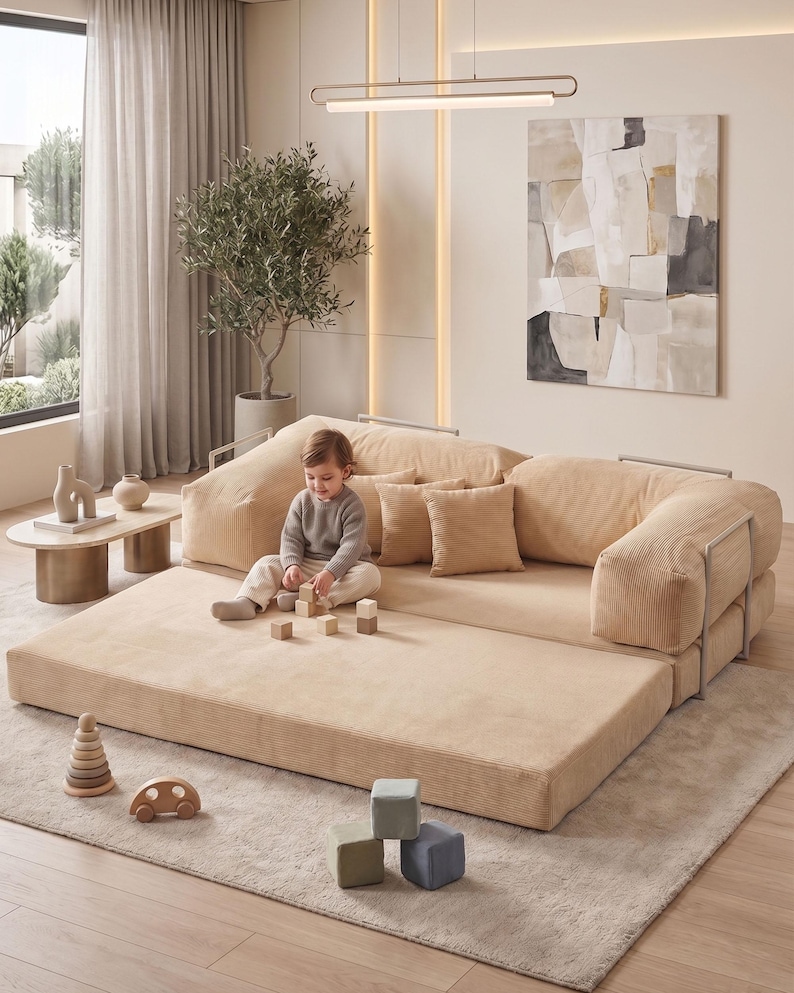 May include: A beige modular sofa with a corduroy texture, featuring a low profile and rounded edges. The sofa is accompanied by matching throw pillows. A child is playing with wooden blocks on the sofa. A wooden toy car and a stacking toy are on the floor.
