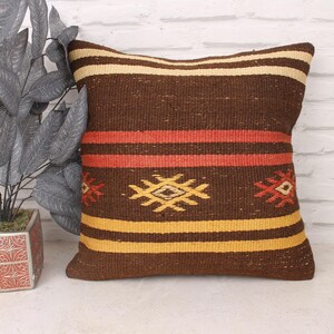 May include: A brown, yellow, and red patterned throw pillow with a geometric design. The pillow is made of woven fabric and has a fringed edge.
