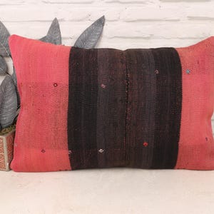 May include: Rectangular decorative pillow with a red and black striped design. The pillow has a red border and a central section of black and dark red stripes. Small, decorative accents are scattered across the surface. The pillow is placed on a white surface.