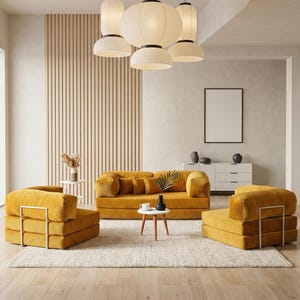 Op de afbeelding: Een moderne woonkamerset met een mosterdgele bank en twee bijpassende fauteuils. De meubels staan op een crèmekleurig tapijt, met een kleine ronde tafel en een witte kast op de achtergrond. Boven hangen papieren lantaarn hanglampen aan het plafond.