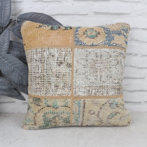 May include: Square decorative pillow with a patchwork design. The pillow features a combination of beige, light blue, and off-white colors. The pillow is made of a woven fabric with a textured appearance. The pillow is approximately 18 inches square.