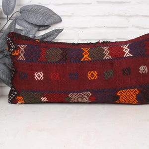 May include: A burgundy rectangular pillow with a colorful geometric pattern. The pillow is made of woven fabric and has a fringed edge.