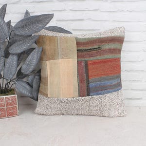 May include: A patchwork cushion with a cream coloured border and a variety of colours and patterns in the centre. The cushion is made of woven fabric and has a rustic, vintage look.