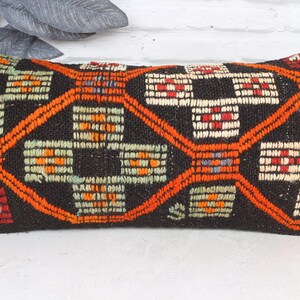 May include: Rectangular decorative pillow with a dark brown background and an intricate geometric pattern in orange, red, and white. The pillow is a home decor item, likely for a sofa or bed.