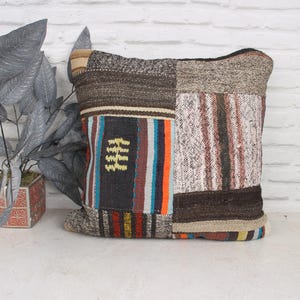 May include: A patchwork pillow with a variety of colors and textures, including brown, beige, orange, blue, and yellow. The pillow is made of woven fabric and has a square shape.