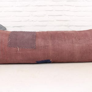 Puede incluir: Una almohada larga y rectangular con un diseño de patchwork. La almohada está hecha de una tela suave y texturizada en tonos de rosa y morado. La almohada es perfecta para agregar un toque de estilo bohemio a cualquier habitación.