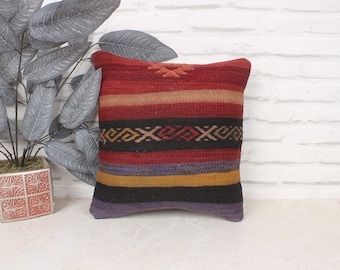 May include: A colorful striped throw pillow with a geometric pattern in shades of red, black, yellow, and blue. The pillow is made of woven fabric and has a fringed edge.
