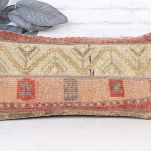 May include: Rectangular decorative pillow with a woven design. The pillow features a beige and peach color scheme with geometric patterns and red accents. The pillow is likely used for home decor.