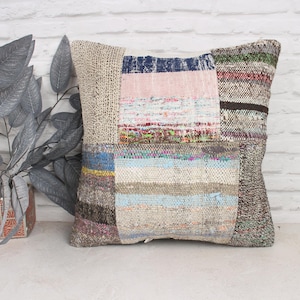 May include: A patchwork pillow cover with a variety of colors and textures, including pink, blue, brown, and white. The pillow cover is made of woven fabric and has a rustic, handmade look.