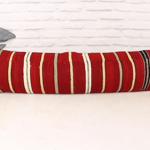 May include: A long, rectangular pillow with a red background and vertical stripes in cream, gray, and black. The pillow is a decorative item, likely for a sofa or bed, and adds a pop of color and pattern to a room.