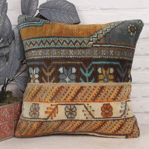 Puede incluir: Un cojín cuadrado decorativo con un diseño estampado. El cojín presenta una mezcla de colores, incluyendo marrón, naranja, turquesa y crema. El diseño incluye formas geométricas y motivos florales, creando una estética vintage o bohemia. Dimensiones: aprox. 40 cm x 40 cm.