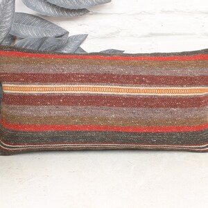 May include: Rectangular pillow with a woven, striped pattern in shades of brown, red, and orange. The pillow has a textured appearance and is designed for decorative use. The pillow is approximately 20 inches long.