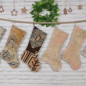 May include: Seven colorful Christmas stockings made from repurposed rugs hang on a white brick wall. The stockings are decorated with various patterns and colors, including blue, brown, pink, and beige.