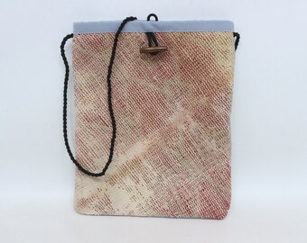 May include: A small, light blue and beige drawstring bag with a black cord and a wooden toggle closure. The bag has a woven texture and a red and yellow pattern.
