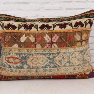 May include: Rectangular decorative pillow with a patchwork design. The pillow features a mix of colors including brown, beige, red, and blue. The design includes floral and geometric patterns, creating a vintage or bohemian aesthetic.