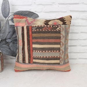 May include: A patchwork pillow cover with a variety of colors and patterns, including red, brown, beige, and gray. The pillow cover is made of woven fabric and has a fringed edge.