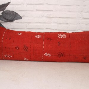 May include: A long, red lumbar pillow with a white and black geometric pattern. The pillow is made of a soft, woven fabric and has a traditional Moroccan design.
