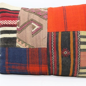 Puede incluir: Una almohada de patchwork con una variedad de patrones y texturas coloridos, incluyendo rojo, naranja, azul y marrón. La almohada está hecha de tejido tejido y tiene una forma rectangular.