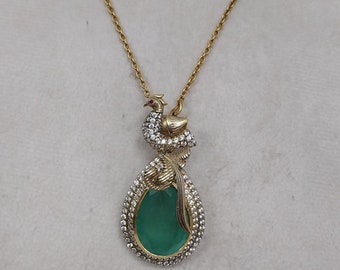 May include: A gold necklace with a green gemstone pendant featuring a jeweled bird design.