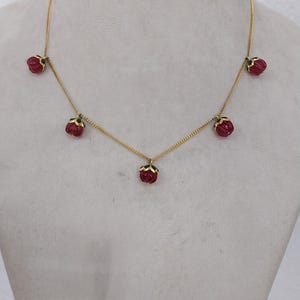 May include: A gold chain necklace with five red flower-shaped pendants.