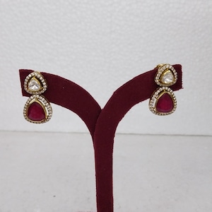 May include: A pair of gold earrings with red and white gemstones. The earrings are on a red velvet stand.