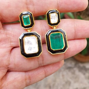 May include: A pair of gold earrings with black enamel and emerald and diamond accents. The earrings are rectangular in shape and have a dangling design.