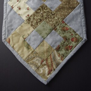 May include: A blue and green patchwork table runner with a paisley design. The runner is made of various fabrics and has a diamond pattern.