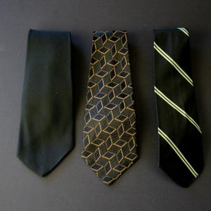 May include: Three neckties are shown against a dark backdrop. The ties include a plain black tie, a patterned tie with a geometric design in black and gold, and a black tie with white diagonal stripes. The ties are arranged vertically.