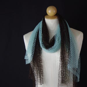 May include: A two-tone scarf on a mannequin. The scarf features a brown and light blue colour scheme, with an open, net-like weave. The scarf is draped to highlight its texture and colour contrast against the white mannequin and black background.