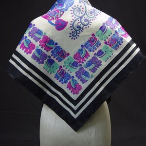May include: A white silk scarf with a black border and a pattern of elephants and paisley designs in shades of blue, pink, and green.